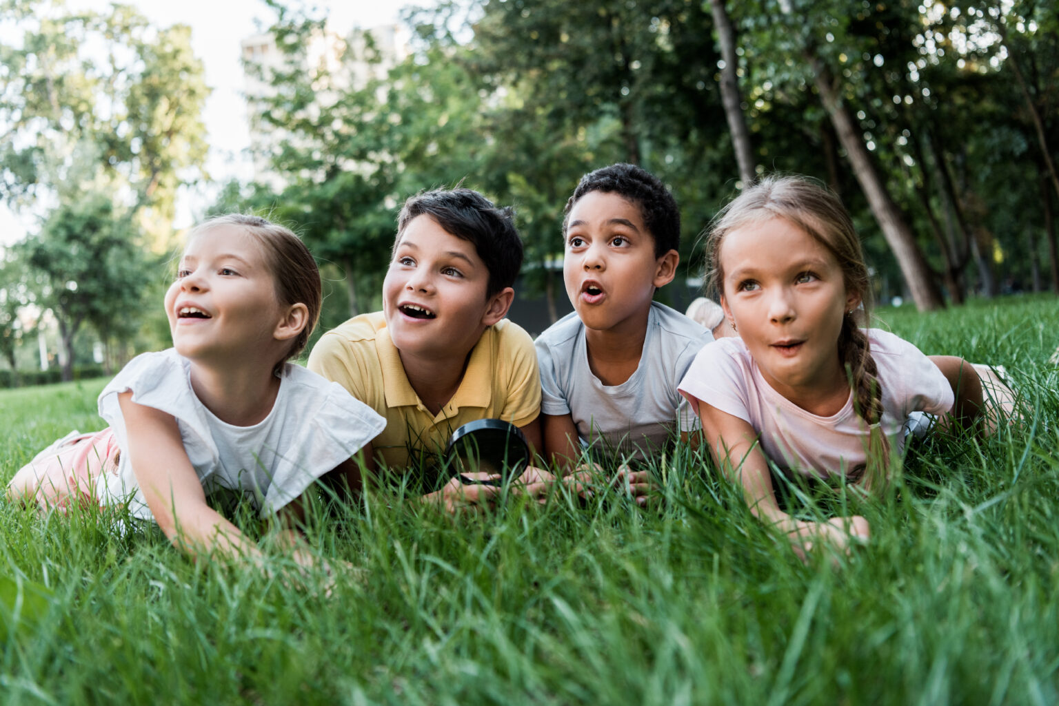 selective focus of surprised multicultural children lying on grass